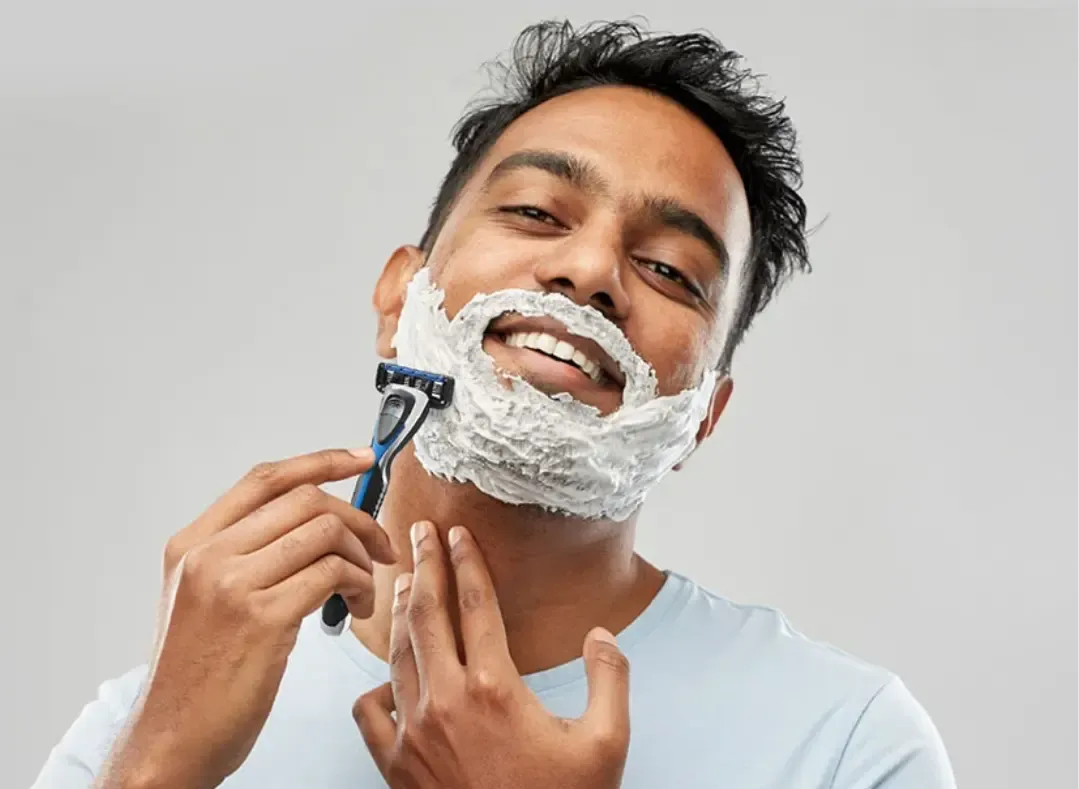 A smiling man shaving with a razor and shaving cream, highlighting a fresh and clean personal care routine.