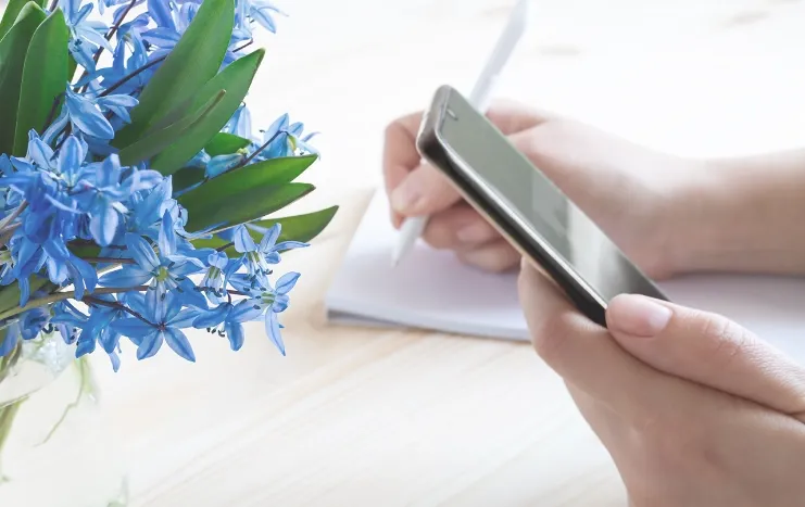 A person holding a smartphone while writing notes, symbolizing Trinergy's seamless mobile digital planning and productivity solutions.