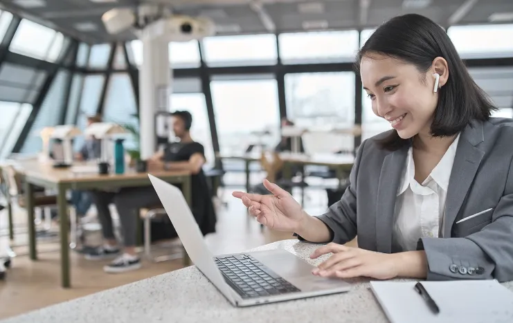 A professional woman using a laptop in a shared workspace, showcasing Trinergy's efficient remote work collaboration solutions.