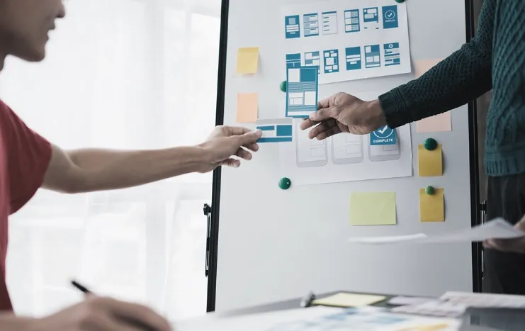 Team collaboration on UI/UX design project, with wireframes and design layouts displayed on a whiteboard.