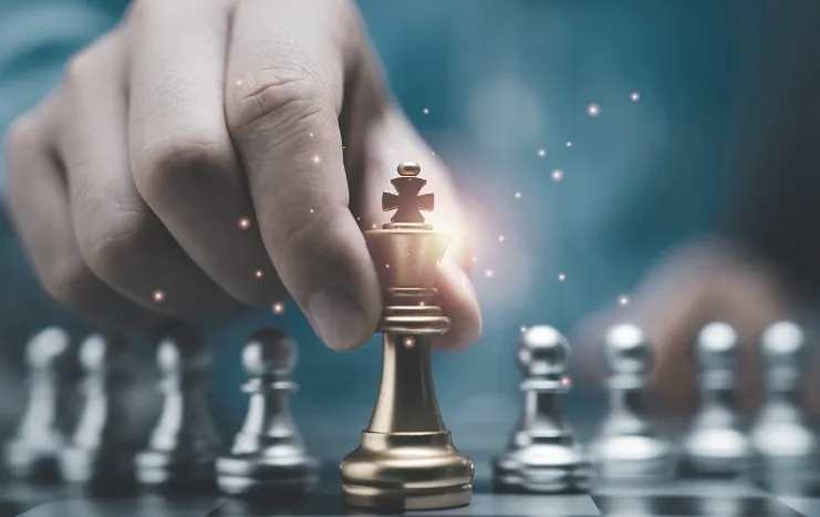 A hand moving a golden chess piece on a chessboard, symbolizing Trinergy's strategic approach to business leadership and success.