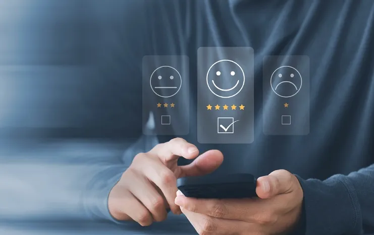 A person using a smartphone with smiley face icons representing a customer feedback system by Trinergy for enhanced user experience.