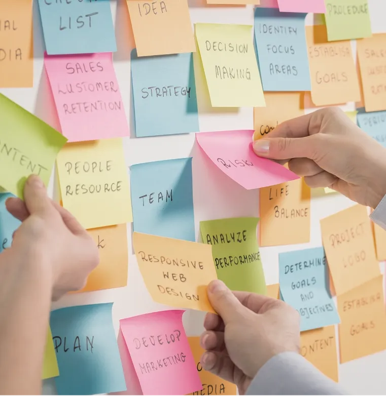 Hands placing sticky notes on a board, representing brainstorming and collaboration during Trinergy’s project sessions.