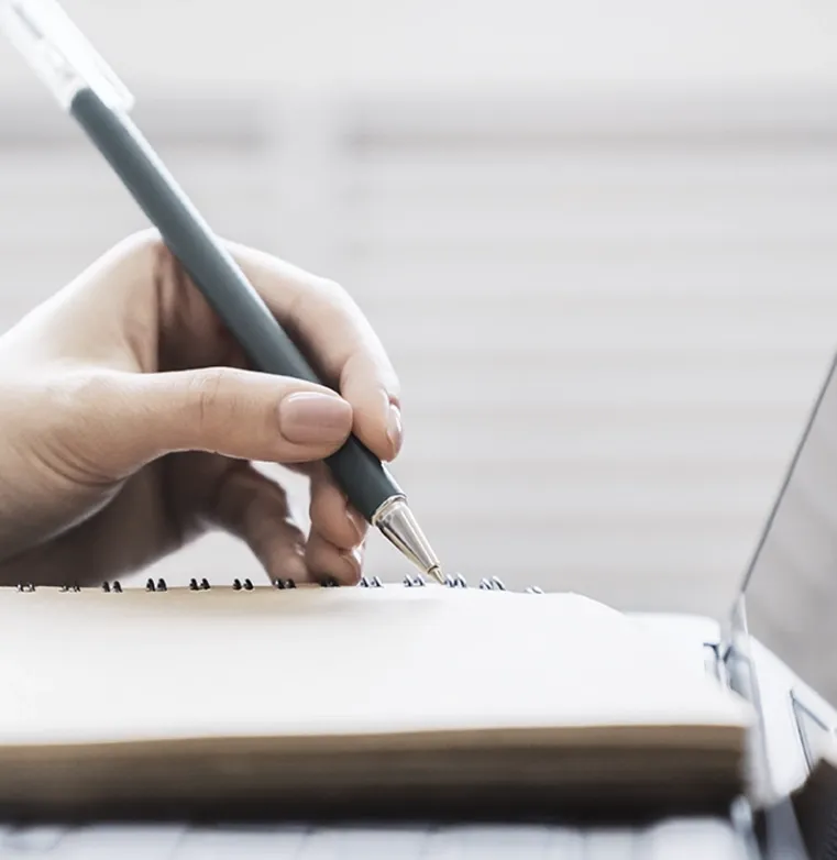 Close-up of a hand writing in a notebook, symbolizing Trinergy's approach to understanding and communicating with clients.